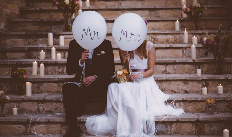 Bride and groom sitting together on rustic staircase and holding balloons